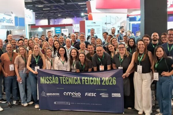 Grande grupo de pessoas da comitiva de Santa Catarina posando com banner da Missão Técnica Feicon 2026. O banner mostra logotipos do Sinduscon Joinville e Amato Negócios como organizadores, e FIESC, Amanco Wavin e Prosul como patrocinadores.
