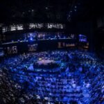 Fotografia panorâmica em ângulo superior da Arena Opus em Santa Catarina durante conferência empresarial. O ambiente apresenta iluminação tecnológica em tons de azul e roxo, com um palco iluminado ao centro e milhares de empreendedores ocupando as galerias e a pista em uma estrutura moderna e imponente.