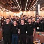 Público geral e organizadores reunidos no palco e na plateia da Growy Immersion na PIB Education, em Itajaí. Jovens universitários, empresários e mentores sorriem e celebram juntos em um auditório moderno com iluminação vibrante de evento corporativo.
