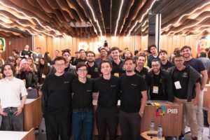 Público geral e organizadores reunidos no palco e na plateia da Growy Immersion na PIB Education, em Itajaí. Jovens universitários, empresários e mentores sorriem e celebram juntos em um auditório moderno com iluminação vibrante de evento corporativo.