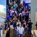 Visão aérea do corredor principal da Feira Construir Aí no Expocentro Balneário Camboriú, mostrando grande movimentação de profissionais, engenheiros, arquitetos e stands modernos do setor da construção civil.