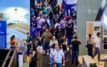 Visão aérea do corredor principal da Feira Construir Aí no Expocentro Balneário Camboriú, mostrando grande movimentação de profissionais, engenheiros, arquitetos e stands modernos do setor da construção civil.