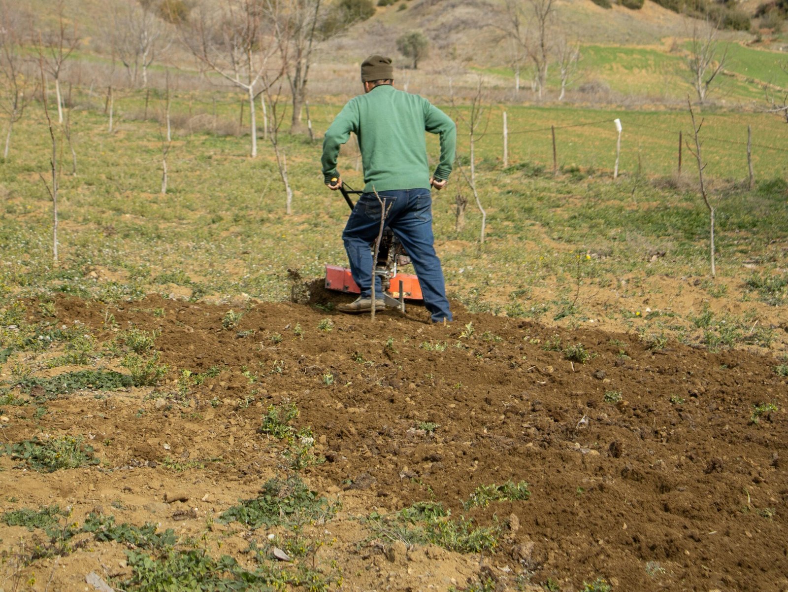 FOI DEMITIDO? SAIBA SEUS DIREITOS - OU SE CABE INDENIZAÇÃO 2 A farmer working with a tiller in an open countryside field, preparing the soil for planting.