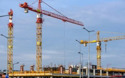 Multiple tower cranes working on a large construction site with blue sky backdrop.